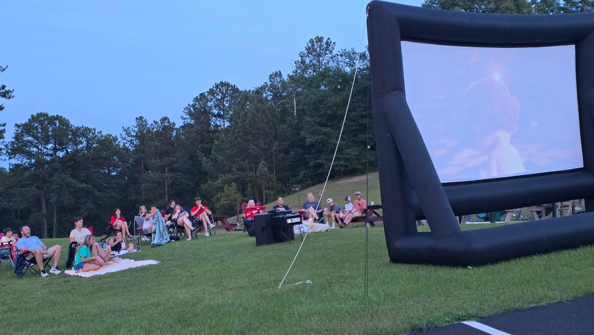 Crowd watching outdoor movie on large inflatable screen at dusk